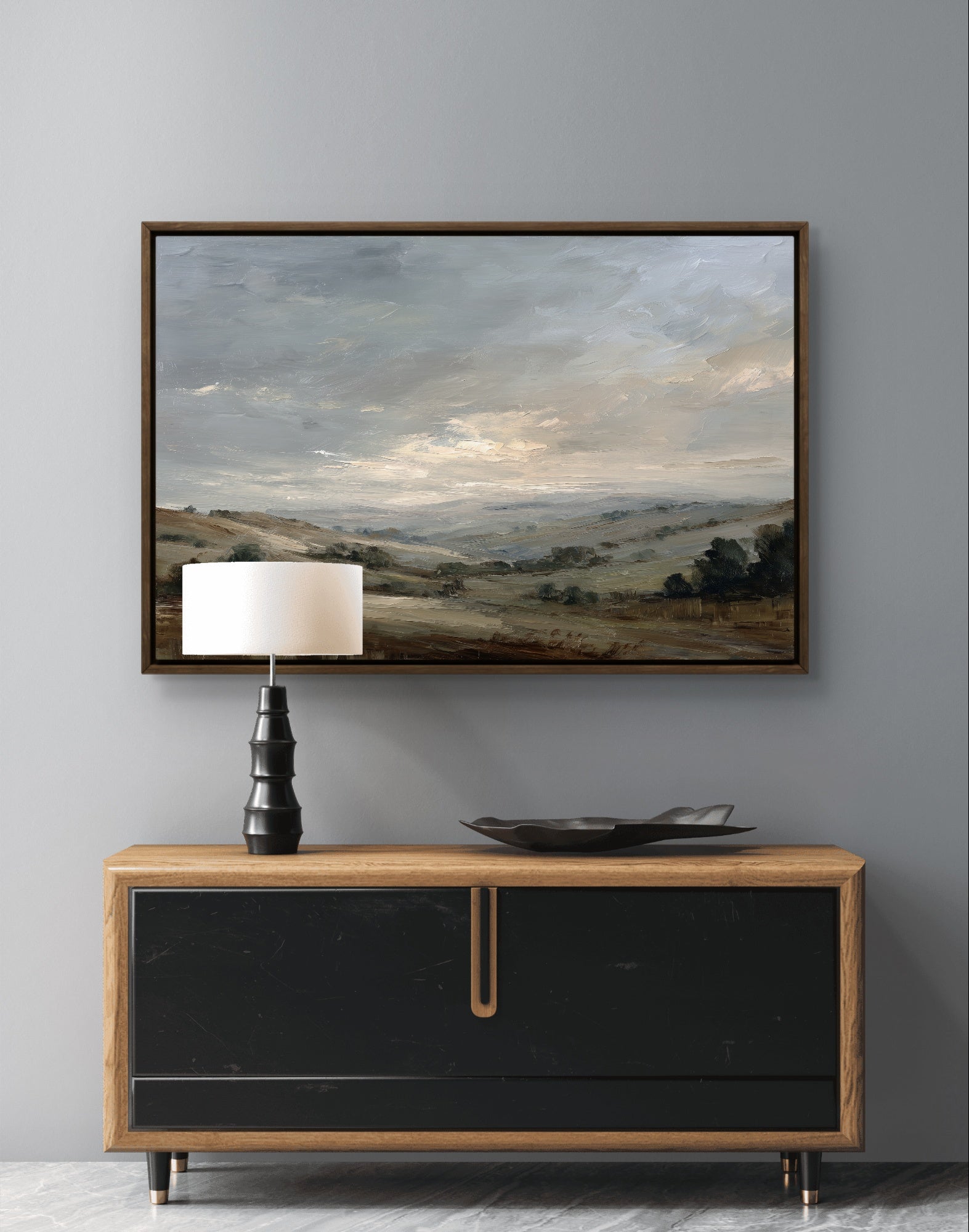 Framed landscape painting above a wooden console table with a lamp and decorative bowl.